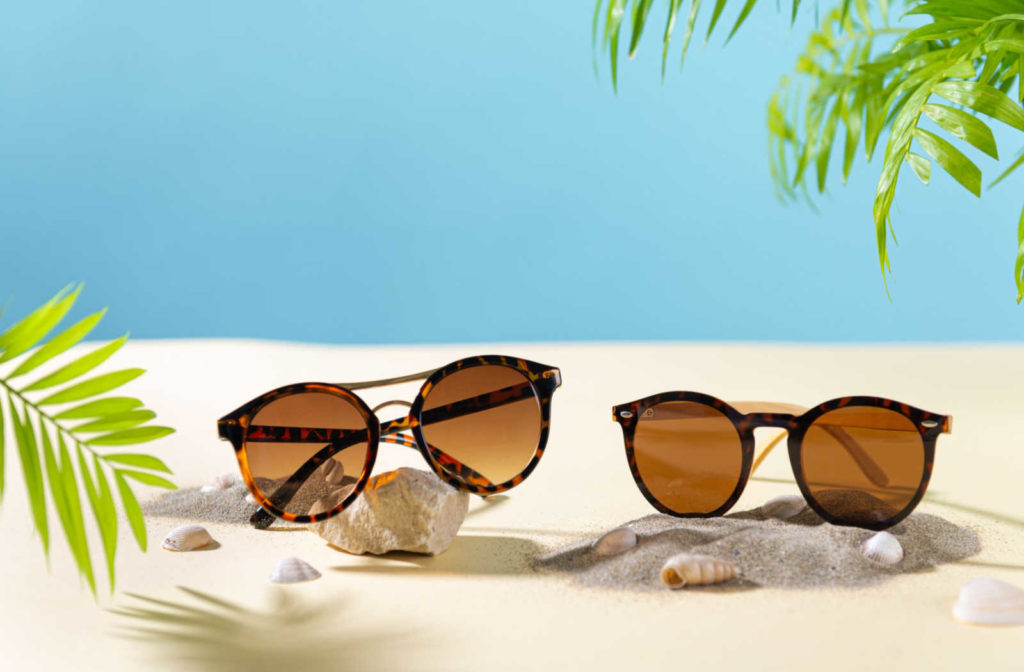 Two pairs of UV sunglasses along a tropical themed backdrop.